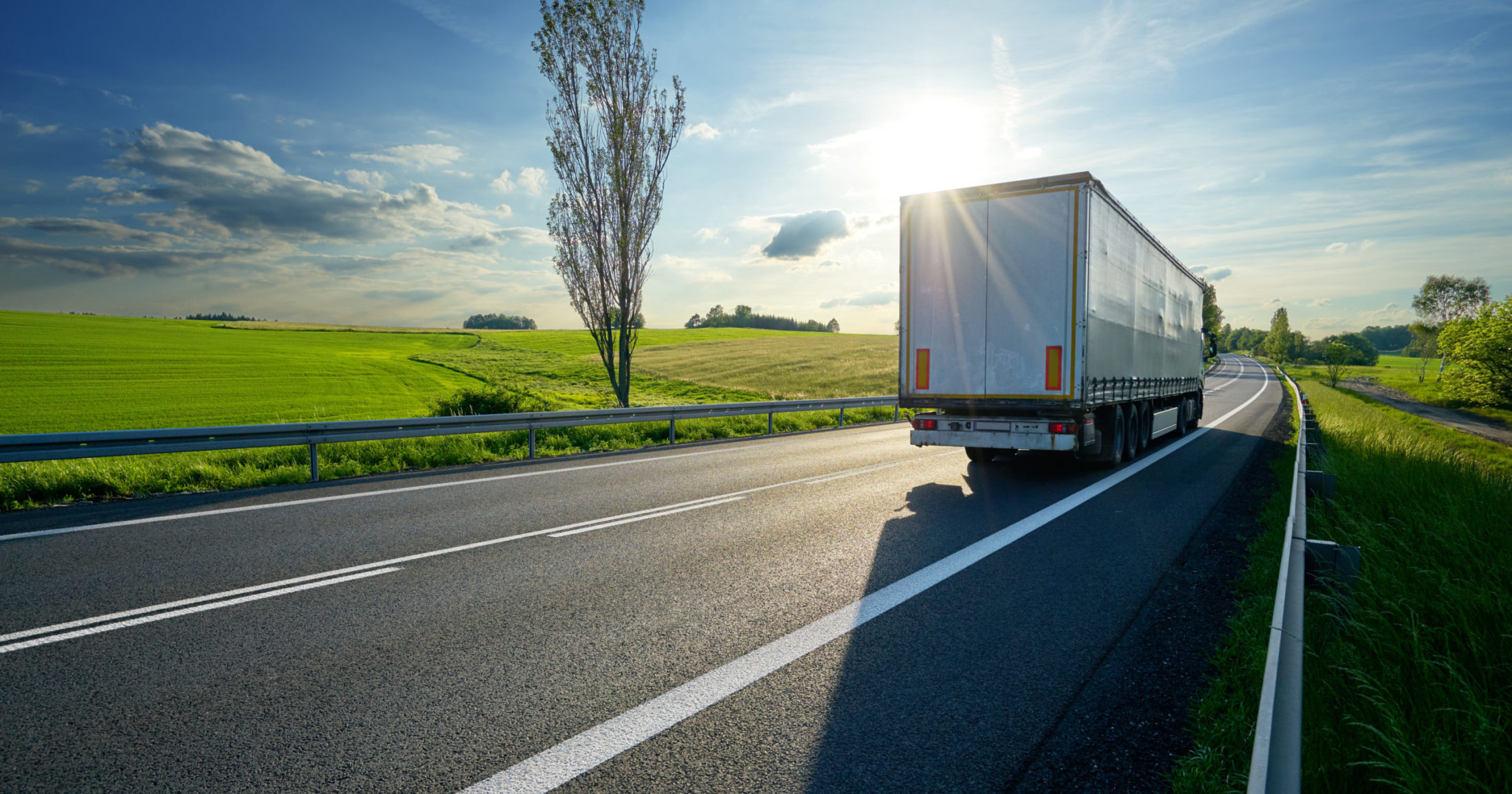 truck driving on asphalt road along the green fields in rural la